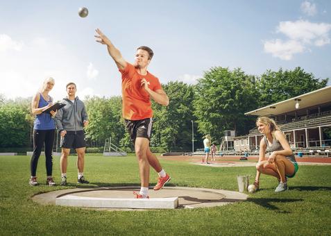 Ein Mann stößt eine Kugel im Stadion, drei Personen beobachten und messen daneben