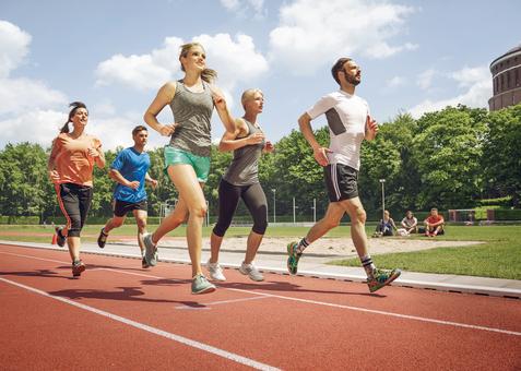 Fünf Erwachsene laufen gemeinsam auf einer Laufbahn im Stadion bei Sonnenschein.