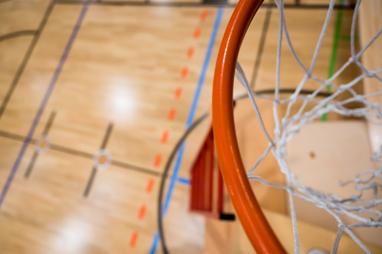 Nahaufnahme eines Basketballkorbs mit Netz über einem aufgezeichneten Basketballfeld aus Holz.