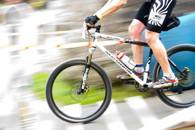 Radsportler fährt mit einem Mountainbike auf einem unebenen Terrain, Wasserflasche am Rahmen, schnelle Bewegung.
