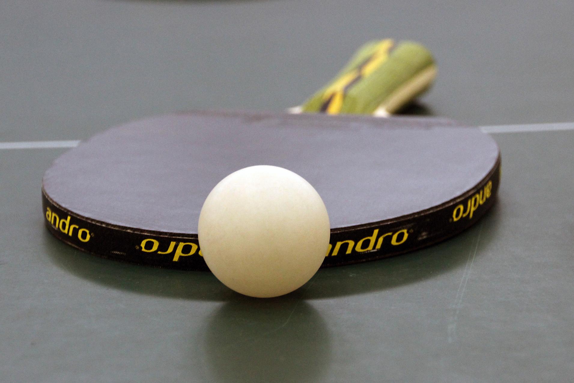 Nahaufnahme eines Tischtennisschlägers mit weißem Ball auf einer grünen Tischtennisplatte.