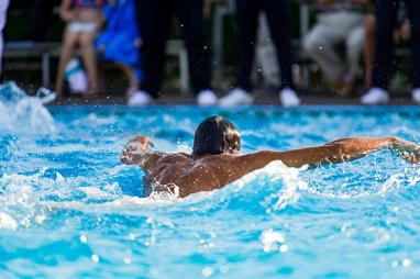 Schwimmer mit freiem Oberkörper, der im Wasser auf dem Rücken schwimmt, umgeben von spritzendem Wasser.